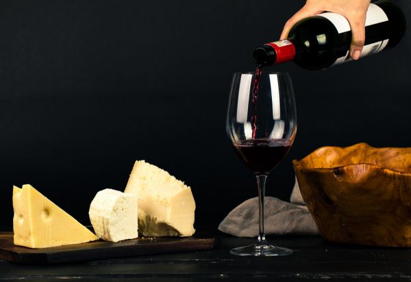 photo of person pouring wine into glass besides some cheese 1545529