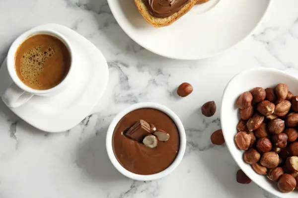Xícara de café ao lado de chocolate e avelãs em composição ilustrativa