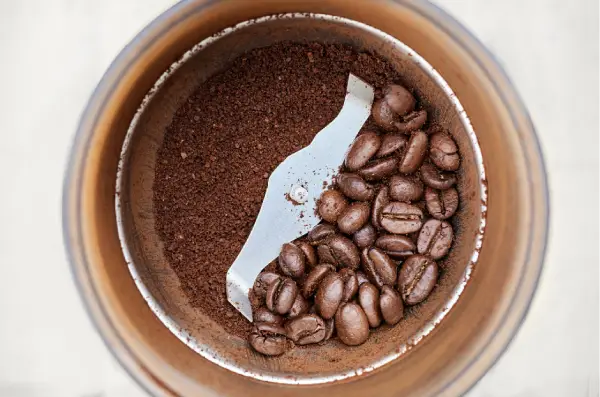 Grãos de café ao lado de um moedor manual
