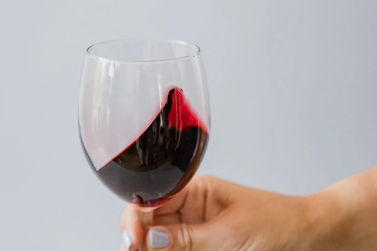 Pessoa degustando Angelica Zapata Merlot 2021 em taça de vinho tinto, na tonalidade indicada pela ficha
