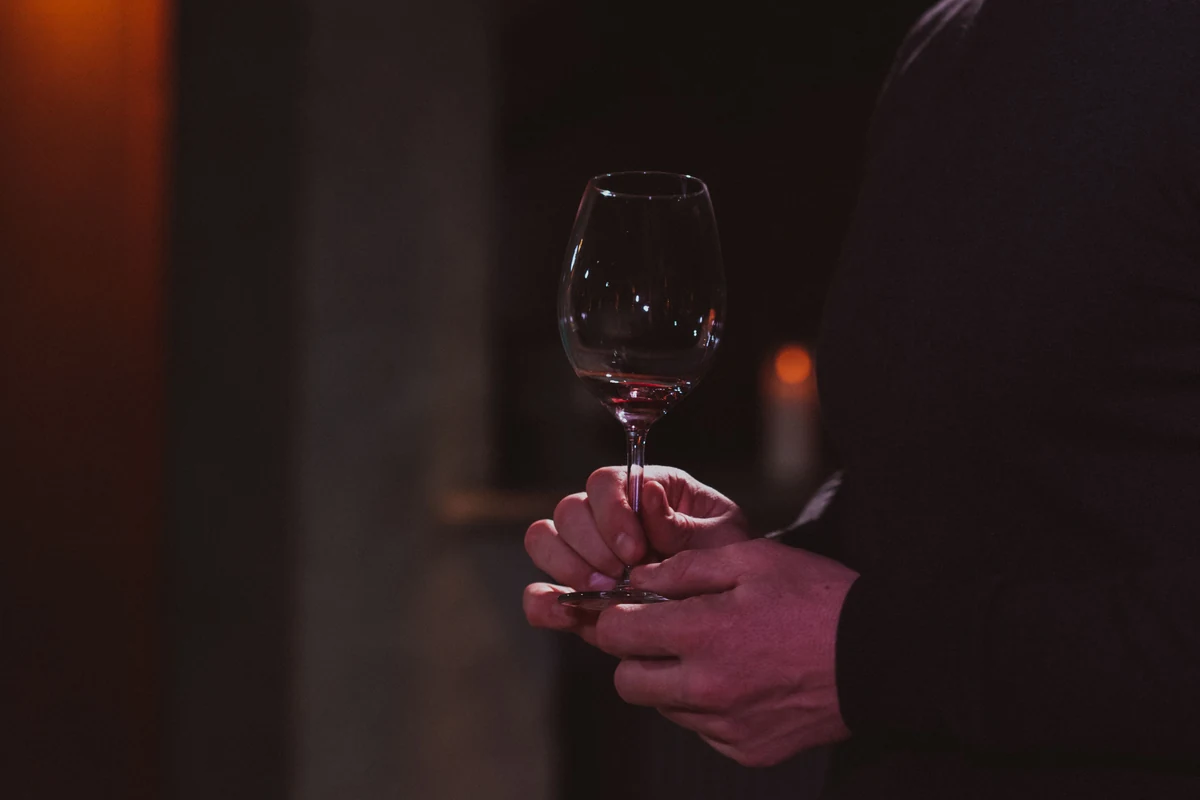 Mãos segurando taça de vinho tinto profundo para representar Beauvignac Merlot Côtes de Thau IGP 2023