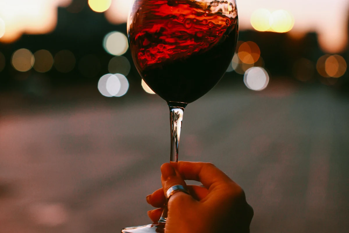 Mão segurando taça de vinho tinto rubi para representar a degustação do Finca Patagonia Single Vineyard Selection Pinot Noir