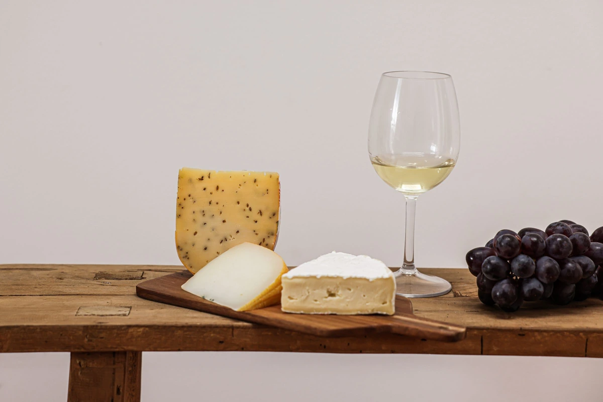 Queijos e uvas ao lado de uma taça de vinho branco