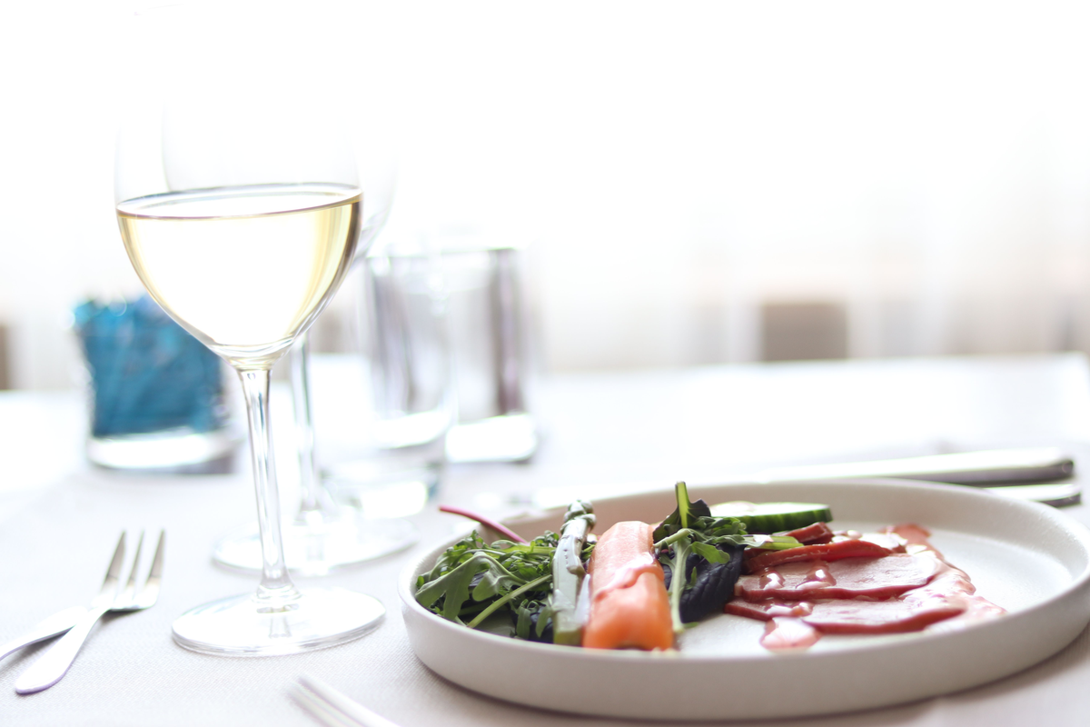 Salada com folhas, pepino e fatias rosadas ao lado de uma taça de vinho branco.