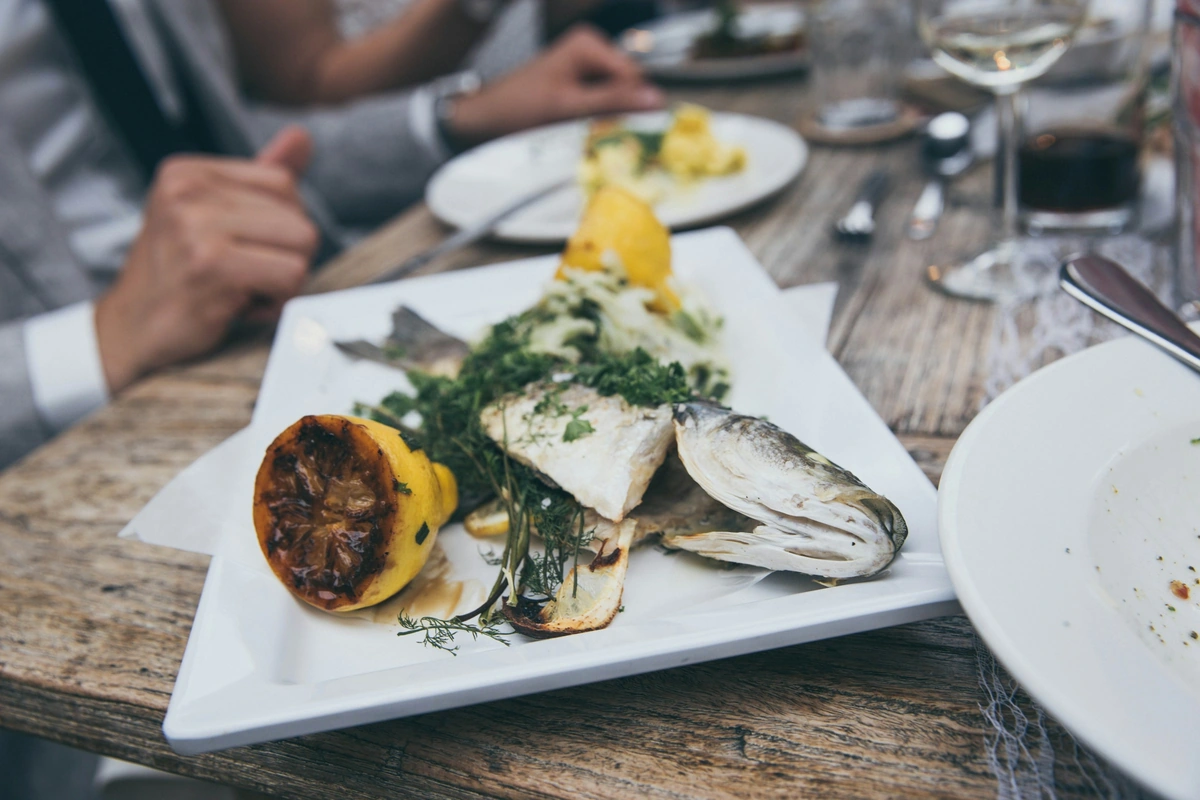 Peixe grelhado com limão e ervas, com taça de vinho branco ao fundo.
