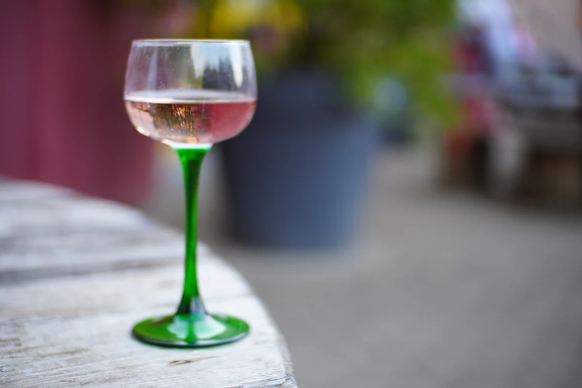 Taça com vinho rosado sobre uma mesa ao ar livre. Fotografia ilustrativa.
