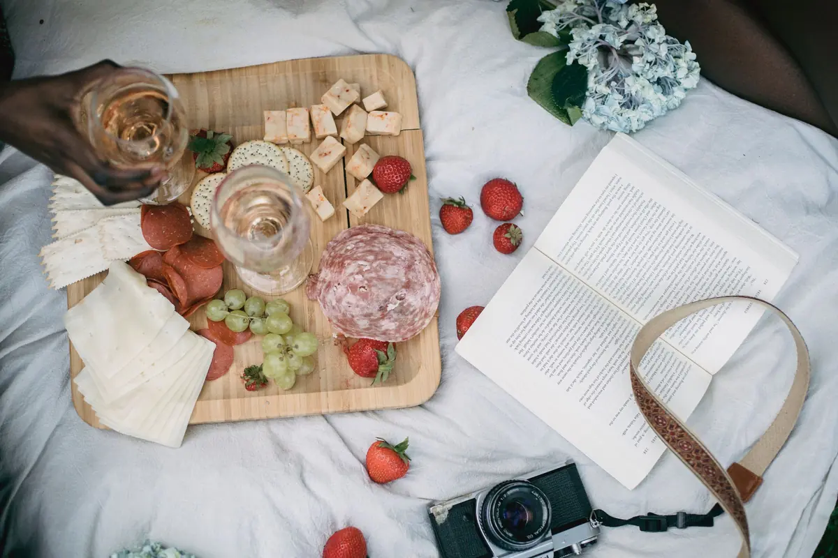 Aperitivos, queijos, frutas e taças de vinho rosado em uma mesa de piquenique. Fotografia ilustrativa.