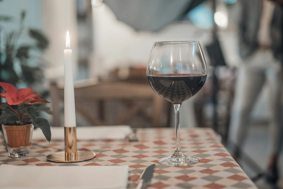 Taça de vinho tinto sobre mesa xadrez ao lado de uma vela