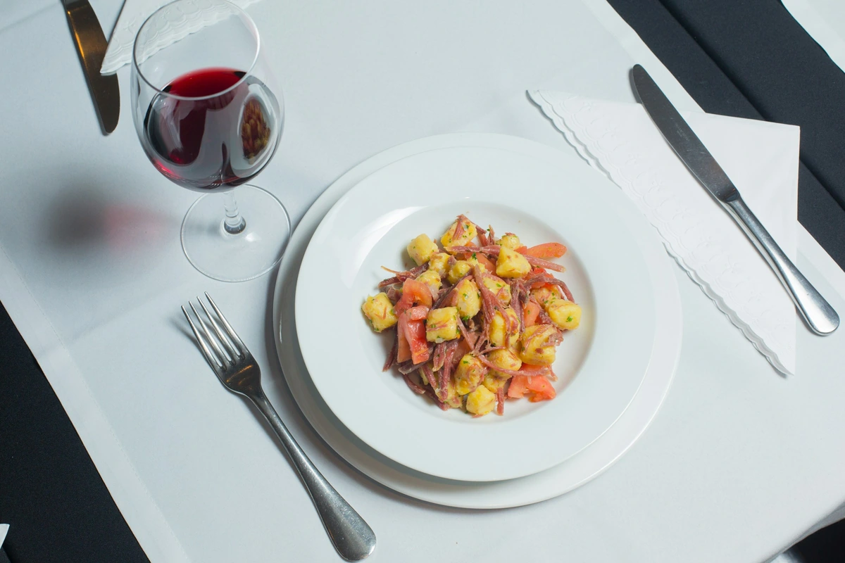 Nhoque com carne e tomate servido ao lado de taça de vinho tinto