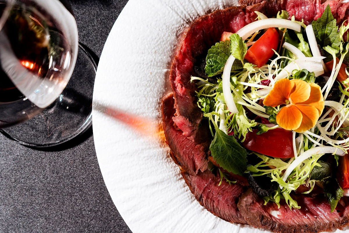 Carpaccio com folhas e uma taça de vinho tinto na mesma mesa. Fotografia ilustrativa.
