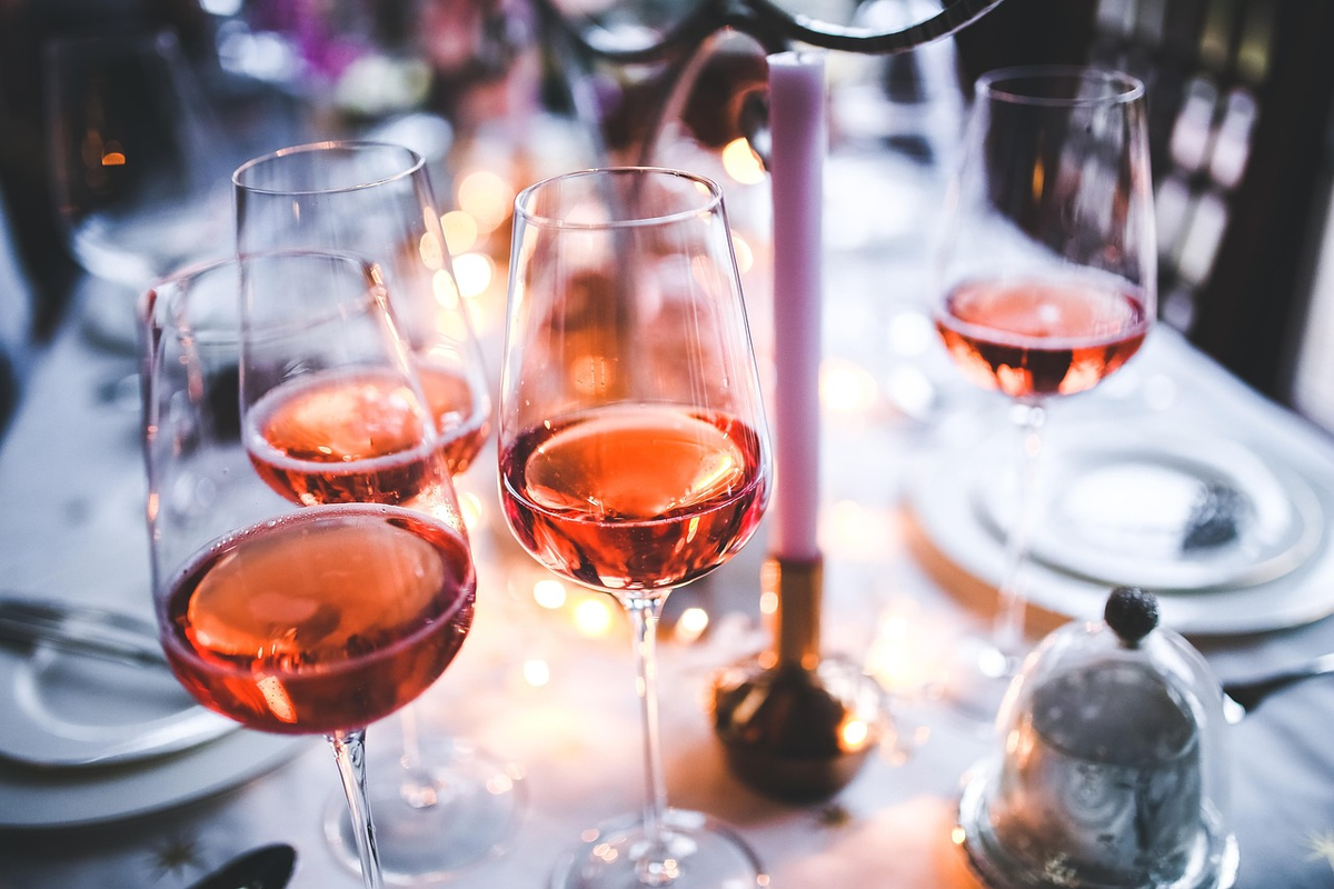 Taças preenchidas de vinho rosé em uma mesa posta para jantar.