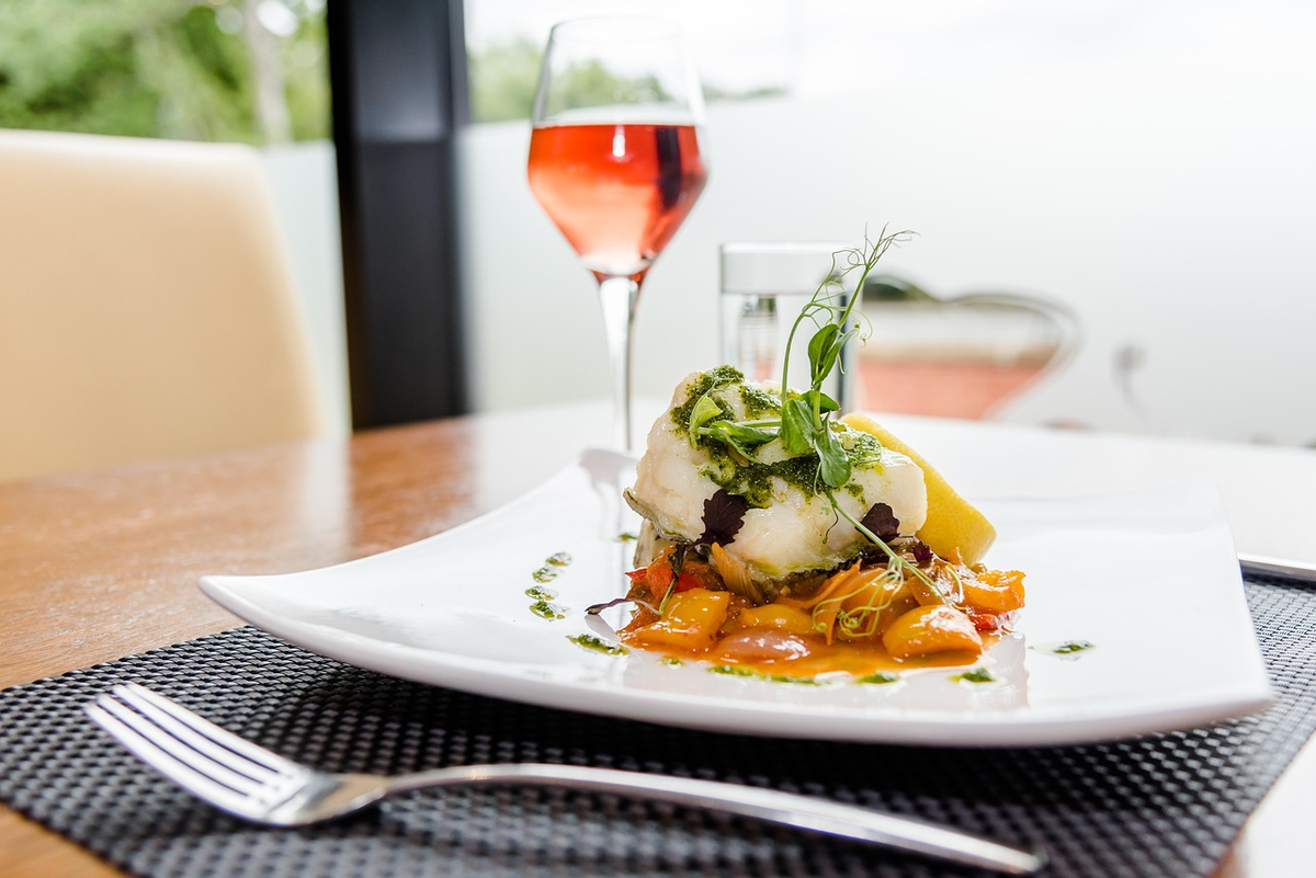Peixe branco com legumes, ervas e limão, acompanhado por uma taça de rosé.