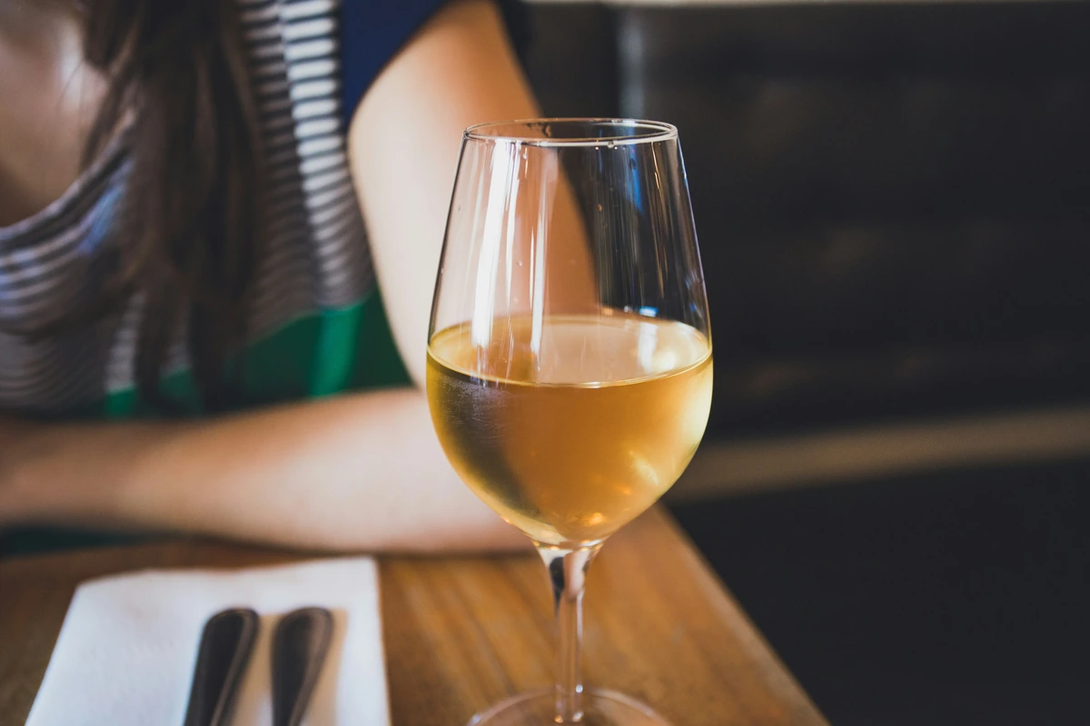 Taça de vinho branco sobre mesa de madeira, em uma refeição compartilhada.
