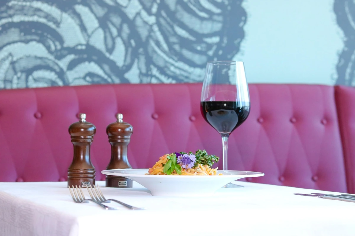 Prato de massa com molho alaranjado e taça de vinho tinto sobre mesa com toalha branca.
