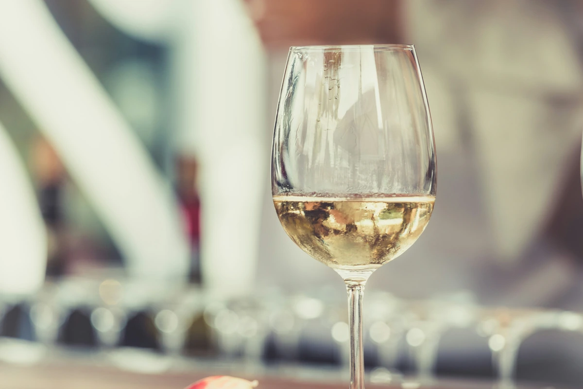Taça com pequena quantidade de vinho branco em ambiente gastronômico luminoso.