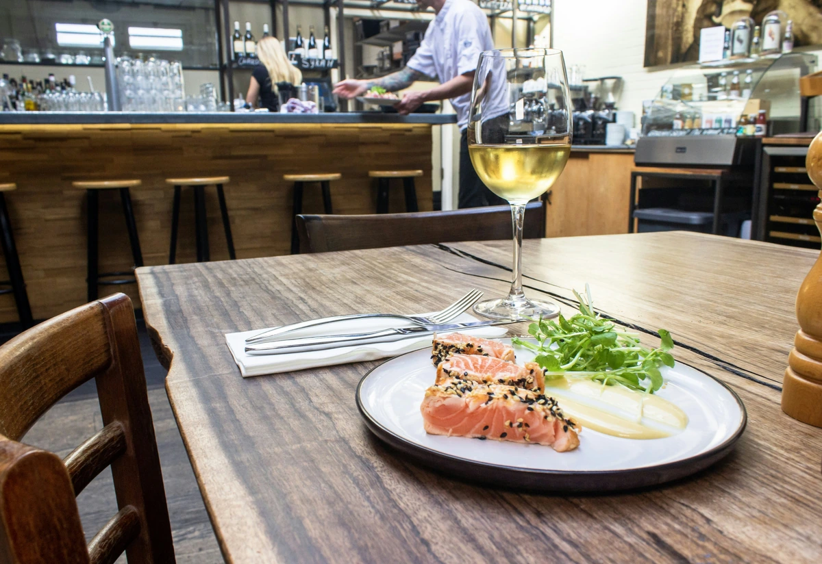 Salmão com gergelim e folhas ao lado de uma taça preenchida de vinho branco.