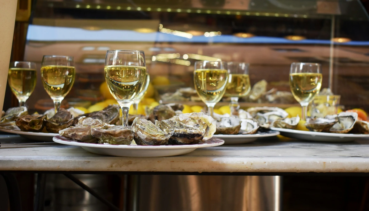 Pratos de ostras e taças preenchidas com vinho branco na mesma mesa.