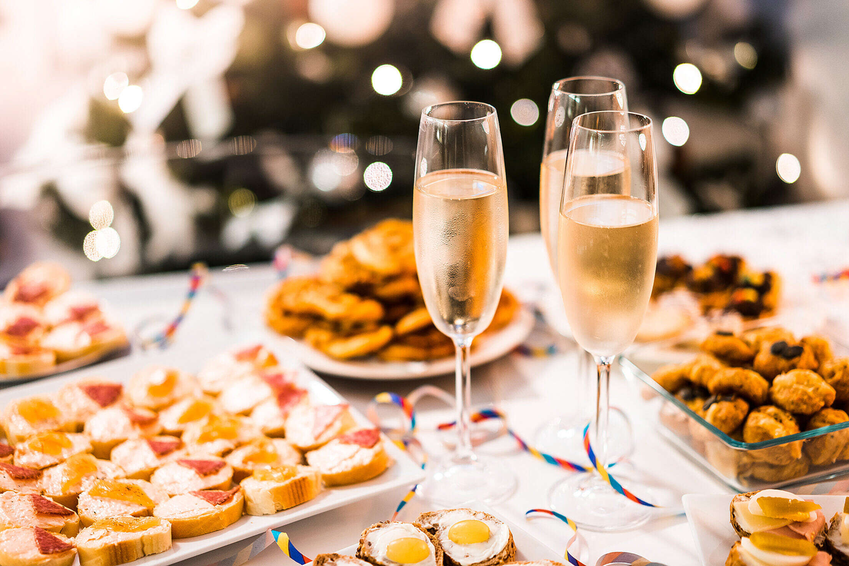 Flûtes com espumante branco entre travessas de canapés e aperitivos salgados.