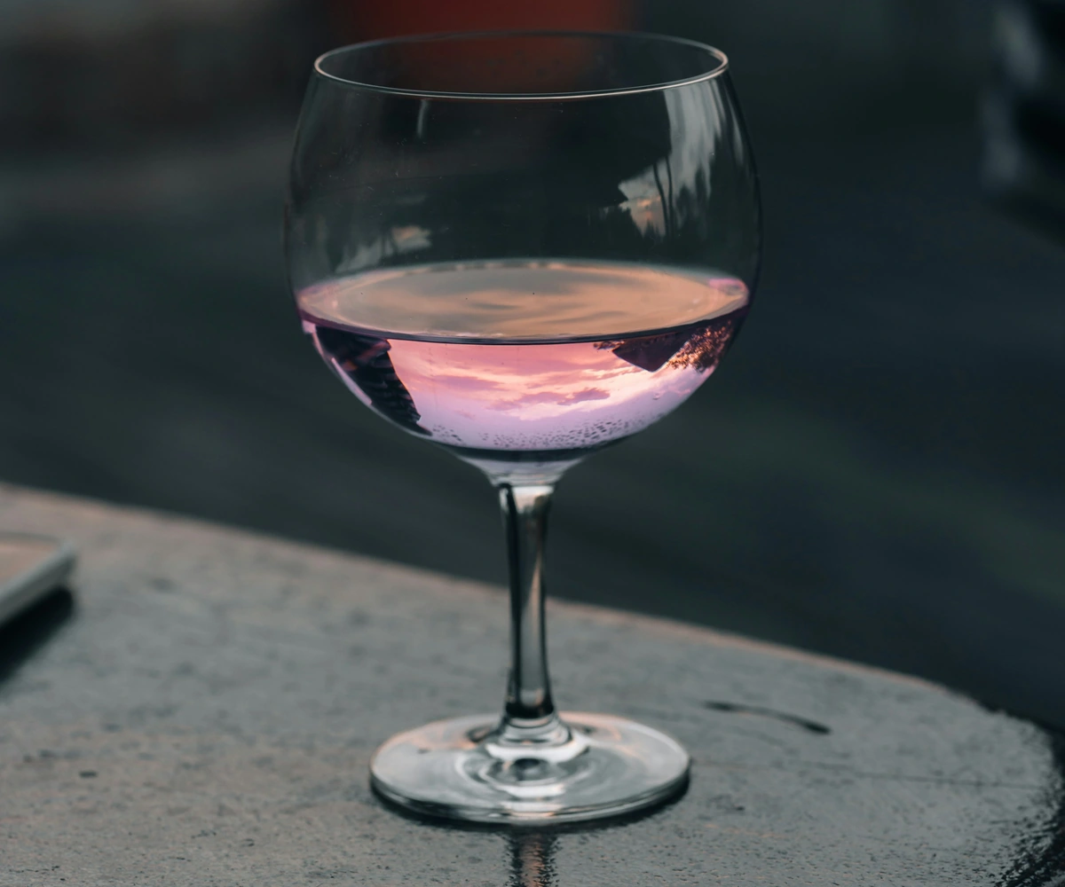 Taça de vinho rosado sobre superfície de pedra, em composição discreta.