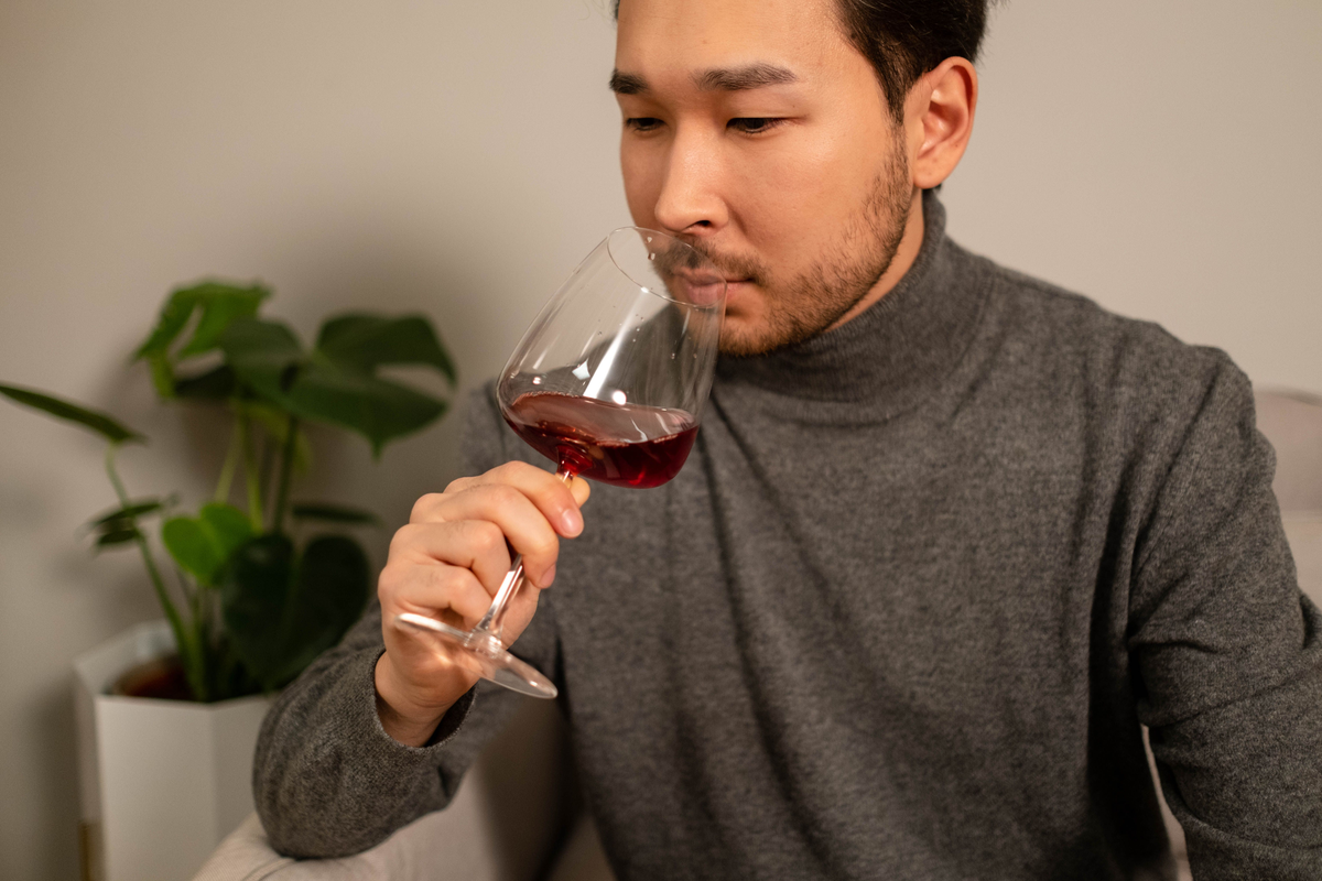 Pessoa sentada aproxima uma taça de vinho tinto do nariz em ambiente doméstico.