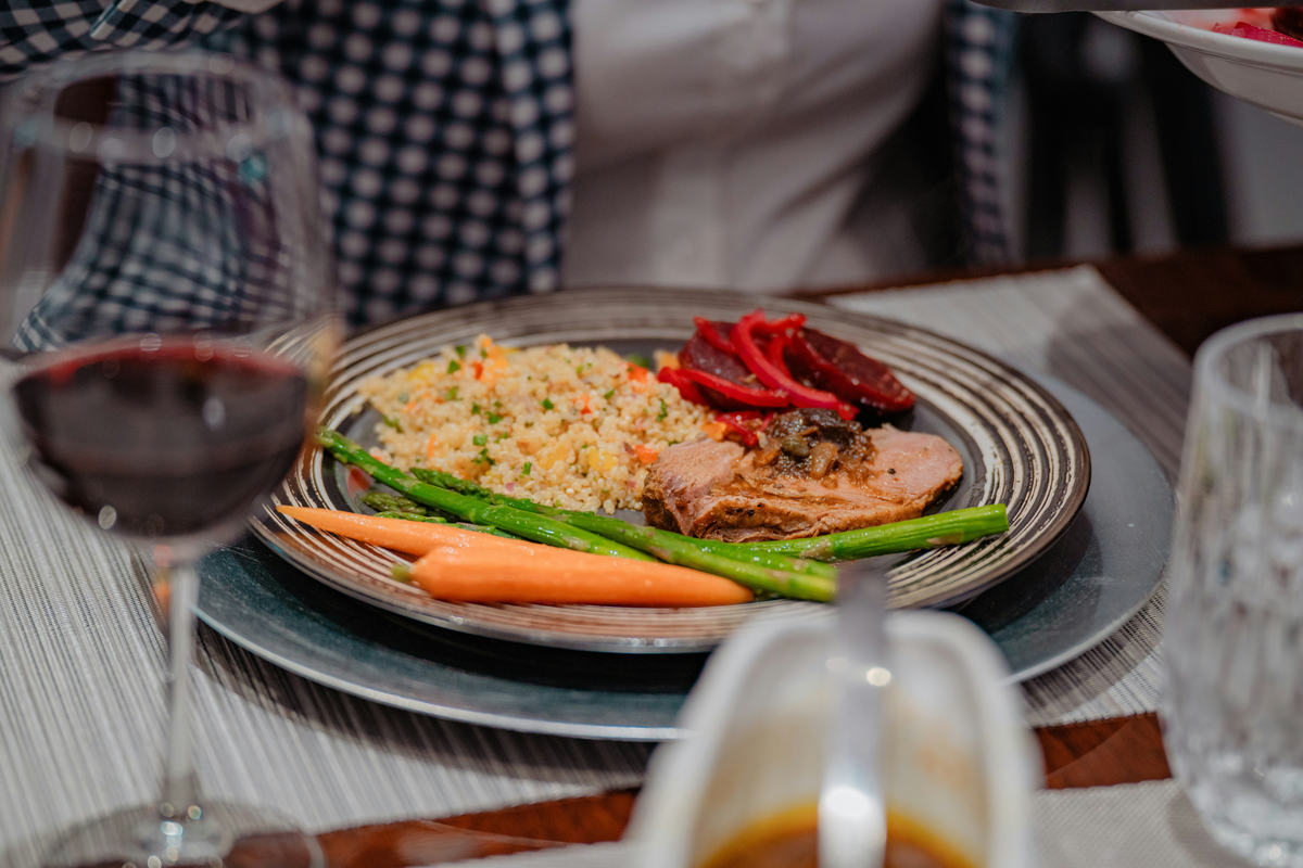 Prato com carne fatiada, grãos e legumes, acompanhado de taça de vinho tinto.