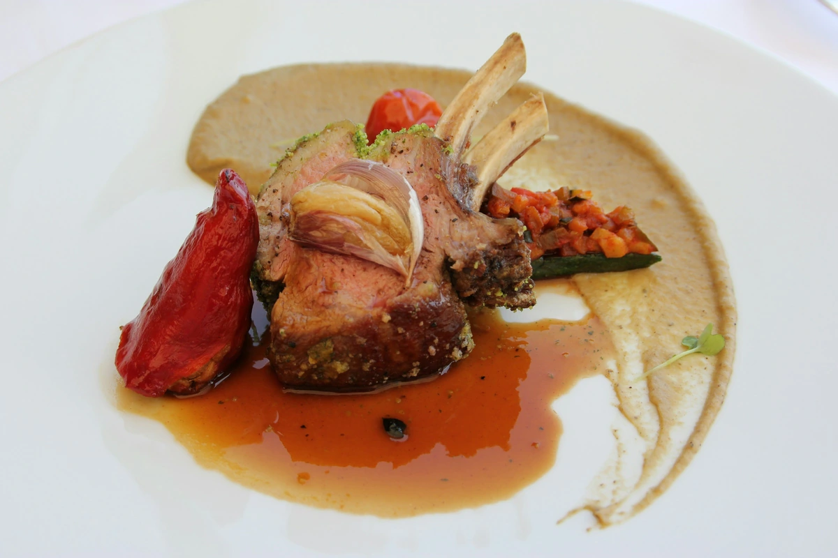 Carré de cordeiro com crosta de ervas, legumes, purê e molho em prato de restaurante