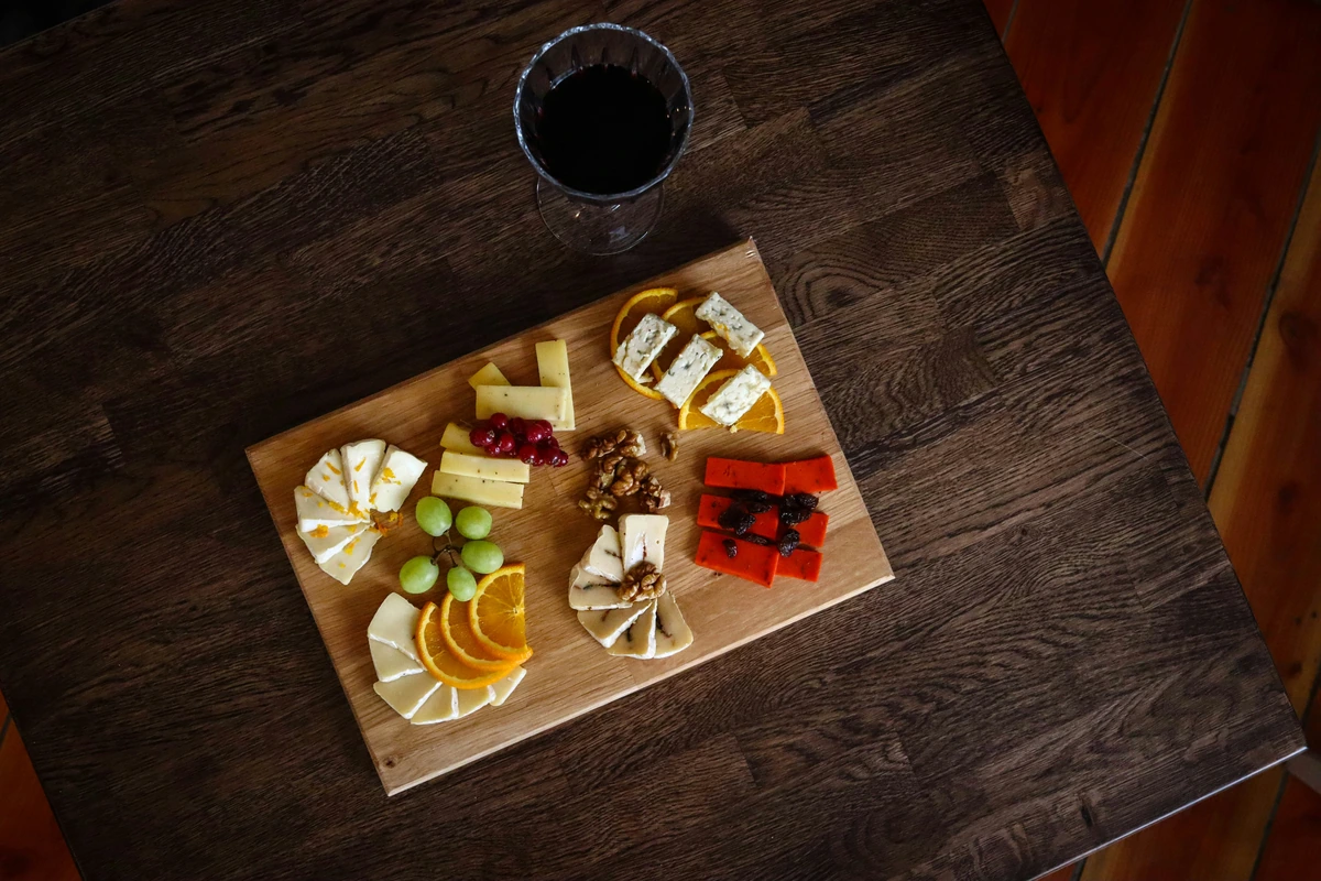 Tábua com queijos, uvas, nozes e frutas acompanhada de taça de vinho tinto.