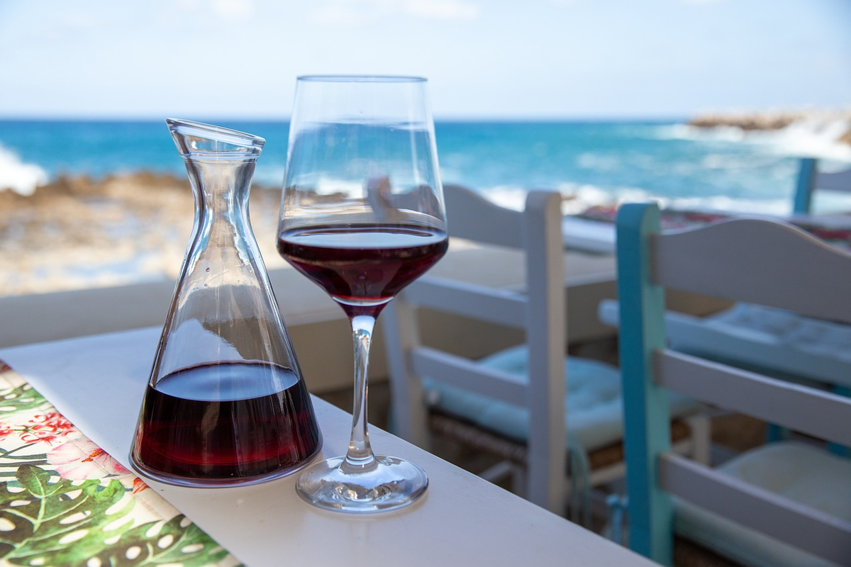 Taça de vinho tinto e pequena jarra de serviço sobre mesa à beira-mar.