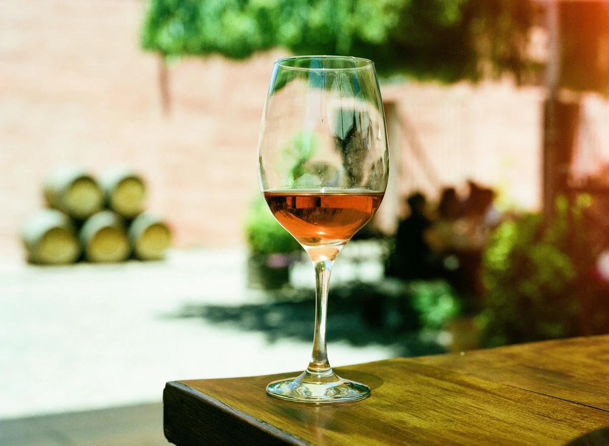 Taça de vinho rosé de tom salmão sobre mesa de madeira ao ar livre.