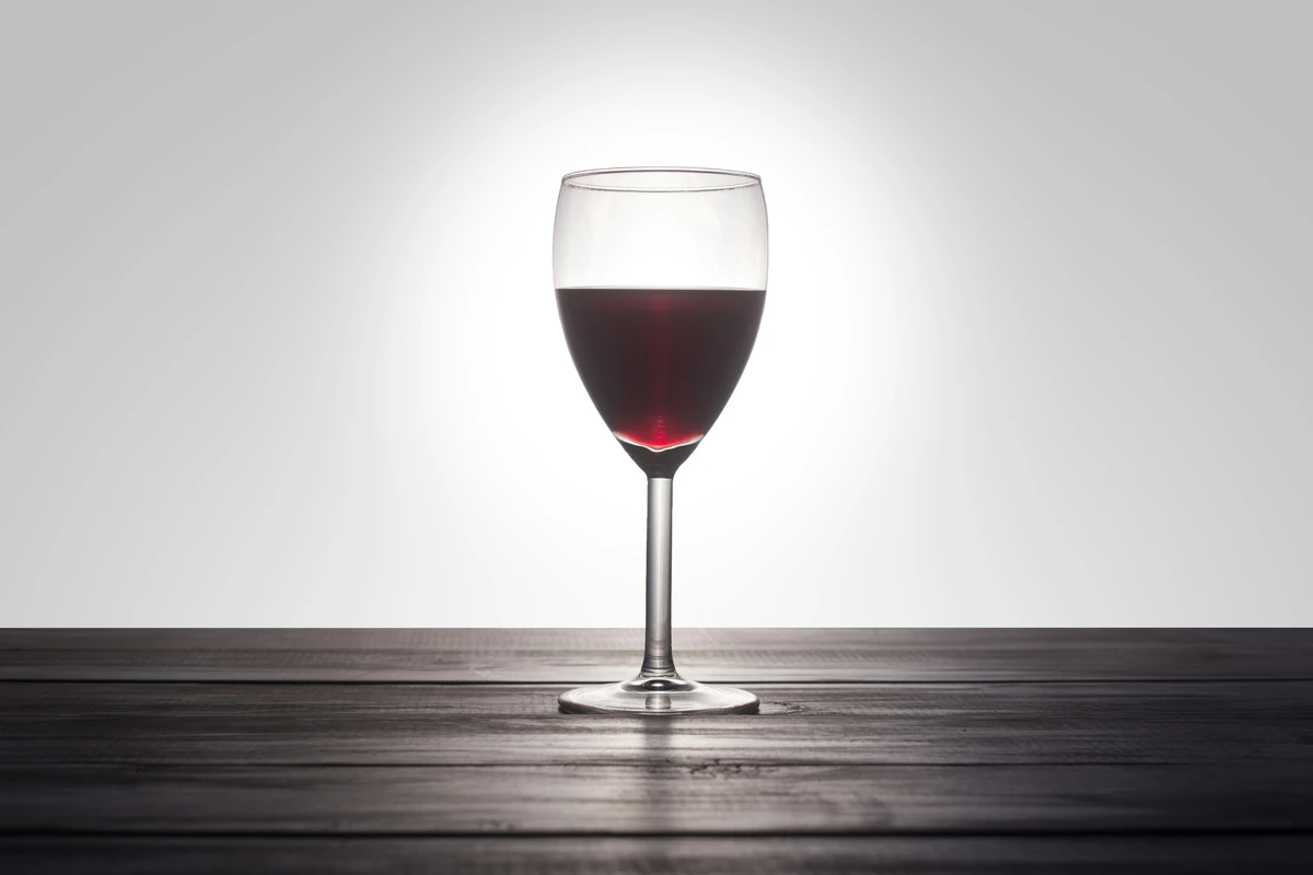 Taça inteira de vinho tinto rubi profundo sobre mesa de madeira escura.