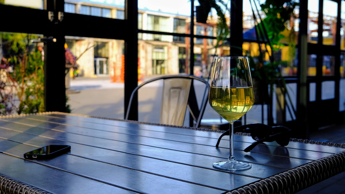 Taça de vinho branco em mesa azulada junto a janelas.
