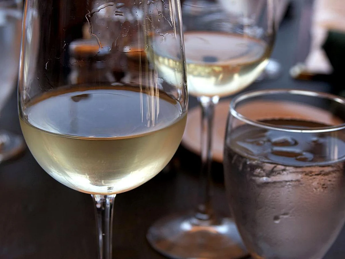 Taça preenchida com vinho branco claro em primeiro plano. Fotografia ilustrativa.