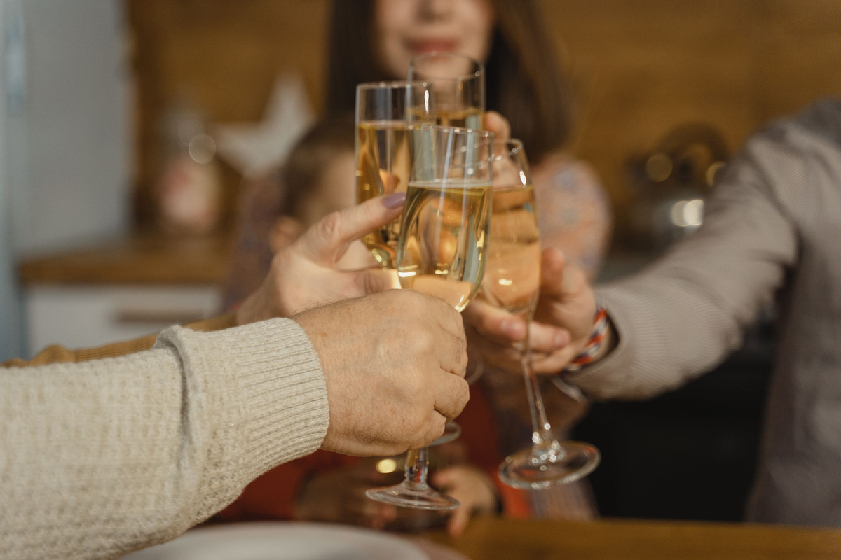 Adultos brindando com flutes de espumante claro em uma mesa acolhedora.