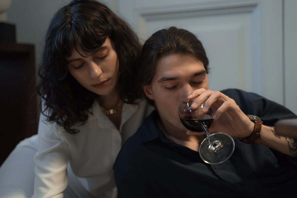 Casal adulto em casa; um homem aprecia uma taça de vinho tinto.