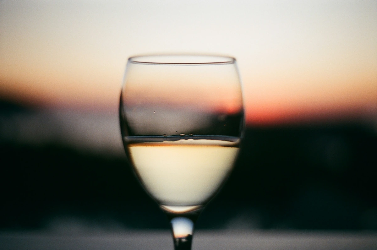 Taça de vinho branco claro diante de um horizonte luminoso.