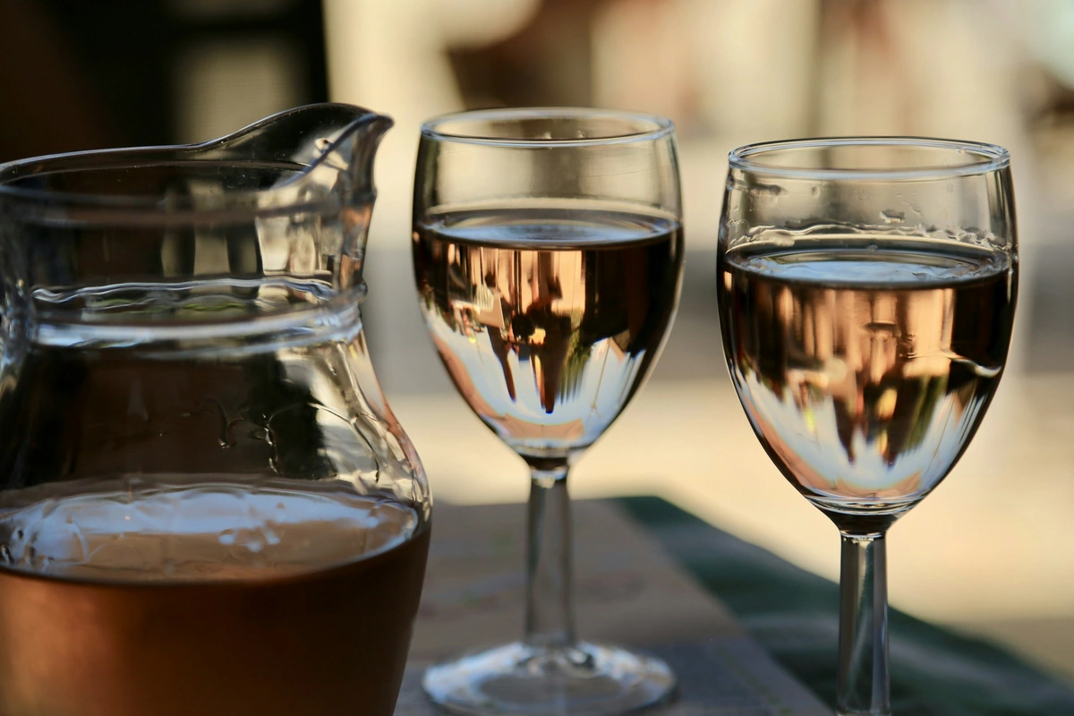 Duas taças com vinho rosado e uma jarra sobre uma mesa externa.