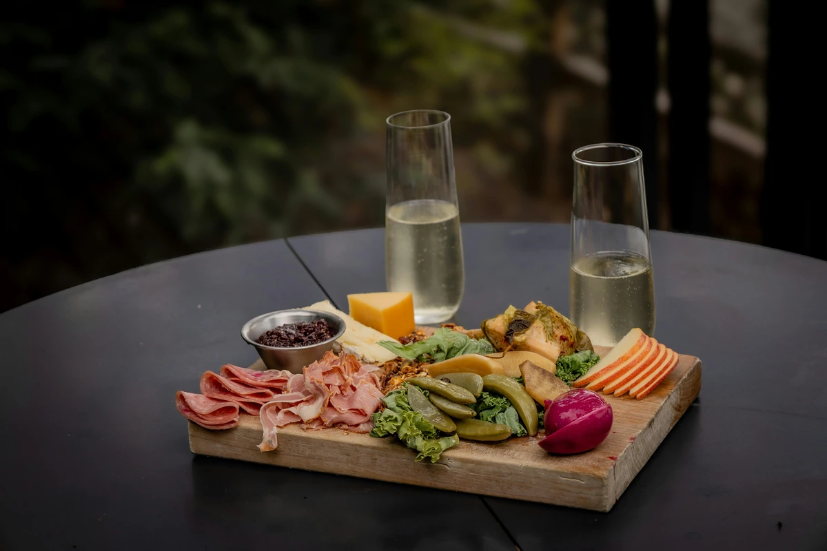 Aperitivos de queijos, carnes curadas e conservas com duas taças preenchidas de espumante branco.