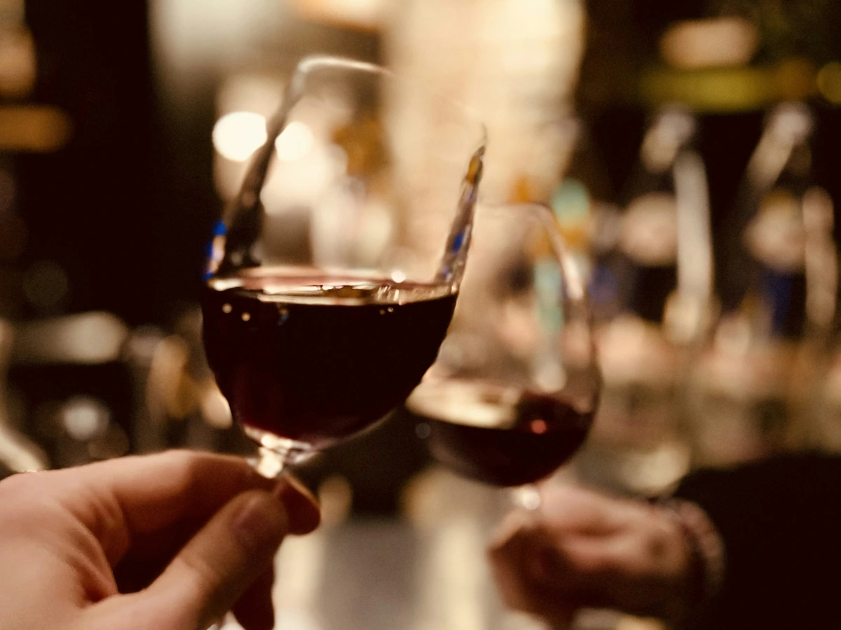 Duas pessoas segurando taças de vinho tinto em um brinde próximo.
