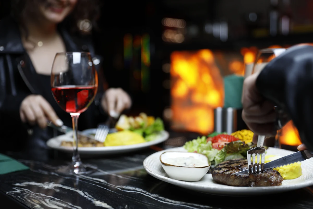 Pratos de carne com acompanhamentos e uma taça de vinho tinto num restaurante.