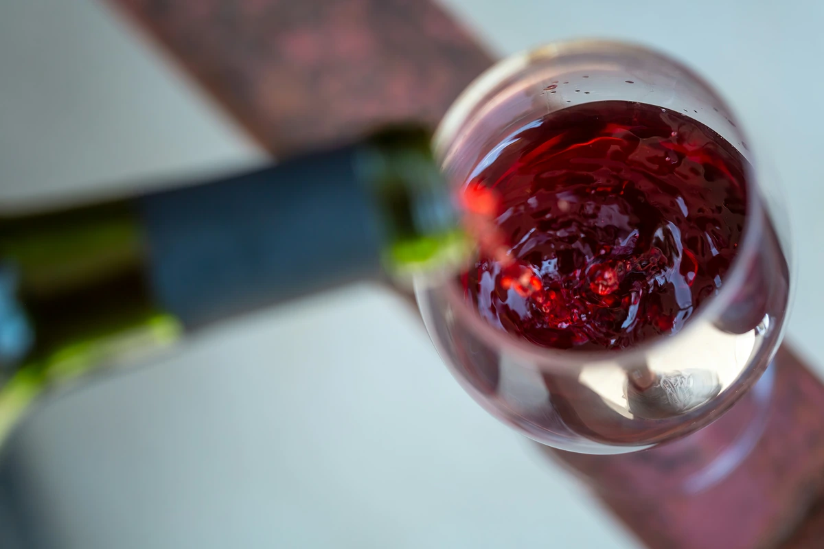 Detalhe de vinho tinto sendo servido em taça ampla, com reflexos rubi e púrpura.
