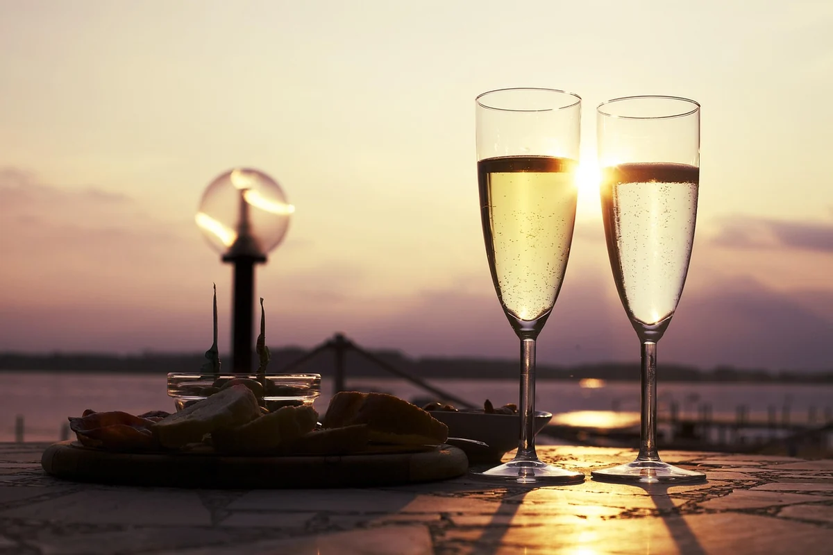 Taças de espumante branco e aperitivos salgados ao entardecer. Fotografia ilustrativa.
