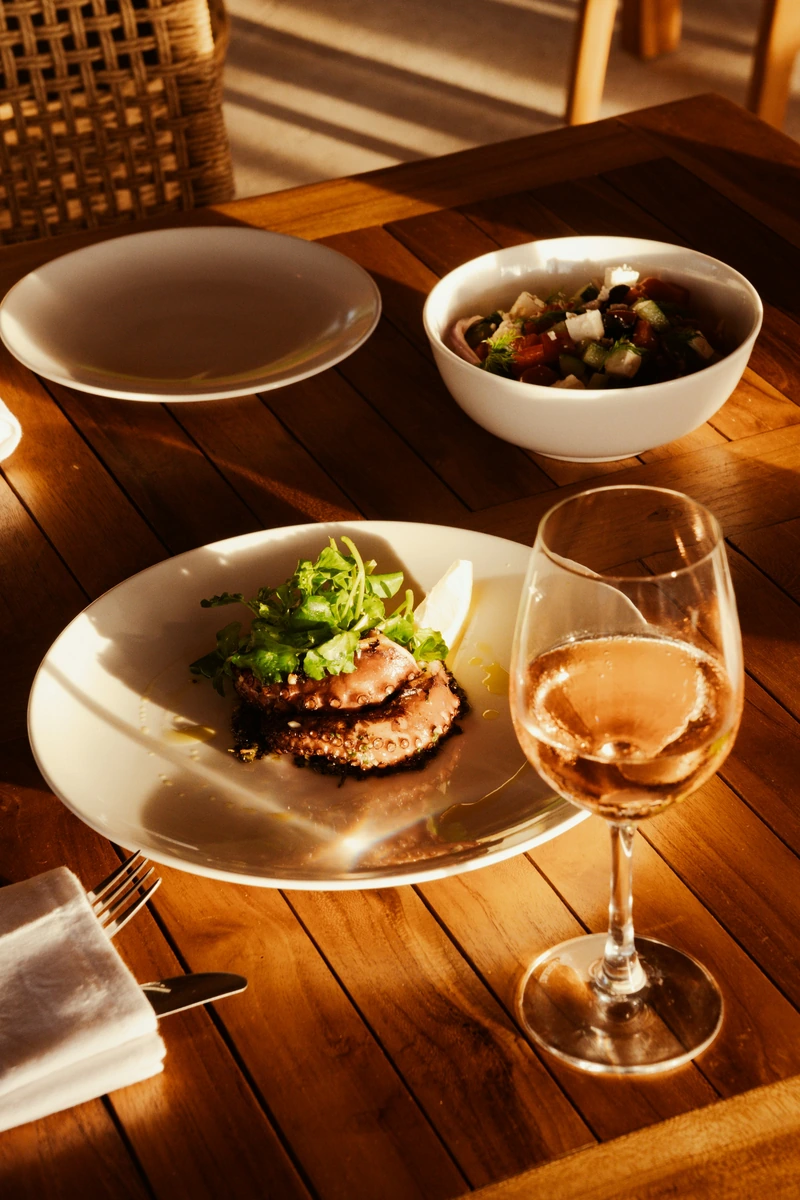 Polvo grelhado com folhas e limão, salada e taça de bebida rosé.