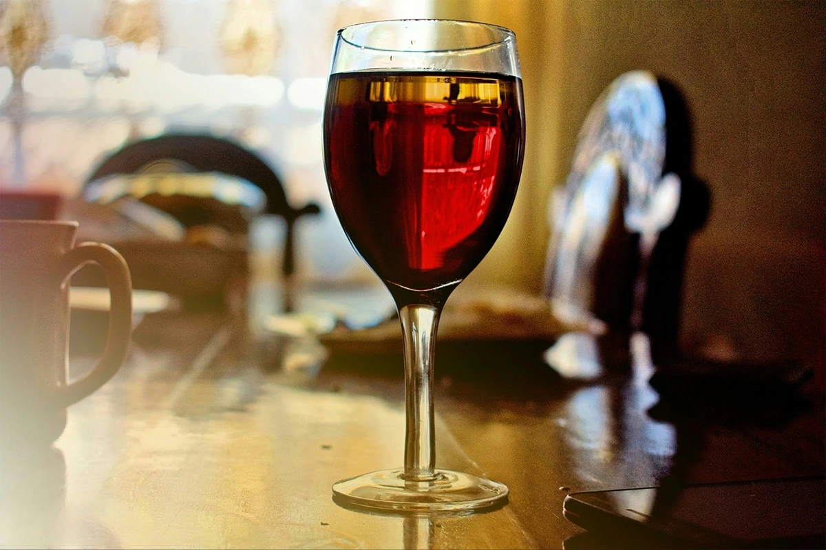 Taça preenchida de vinho tinto sobre mesa de madeira em ambiente acolhedor.