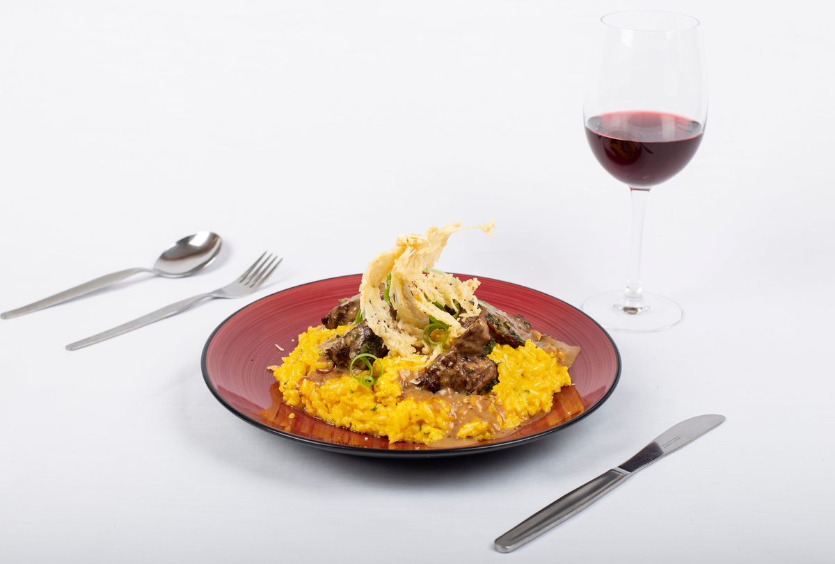 Prato com arroz amarelo, carne e guarnição crocante ao lado de uma taça de vinho tinto.