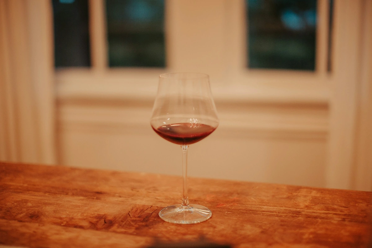 Taça ampla com pequena dose de vinho tinto translúcido sobre uma mesa de madeira