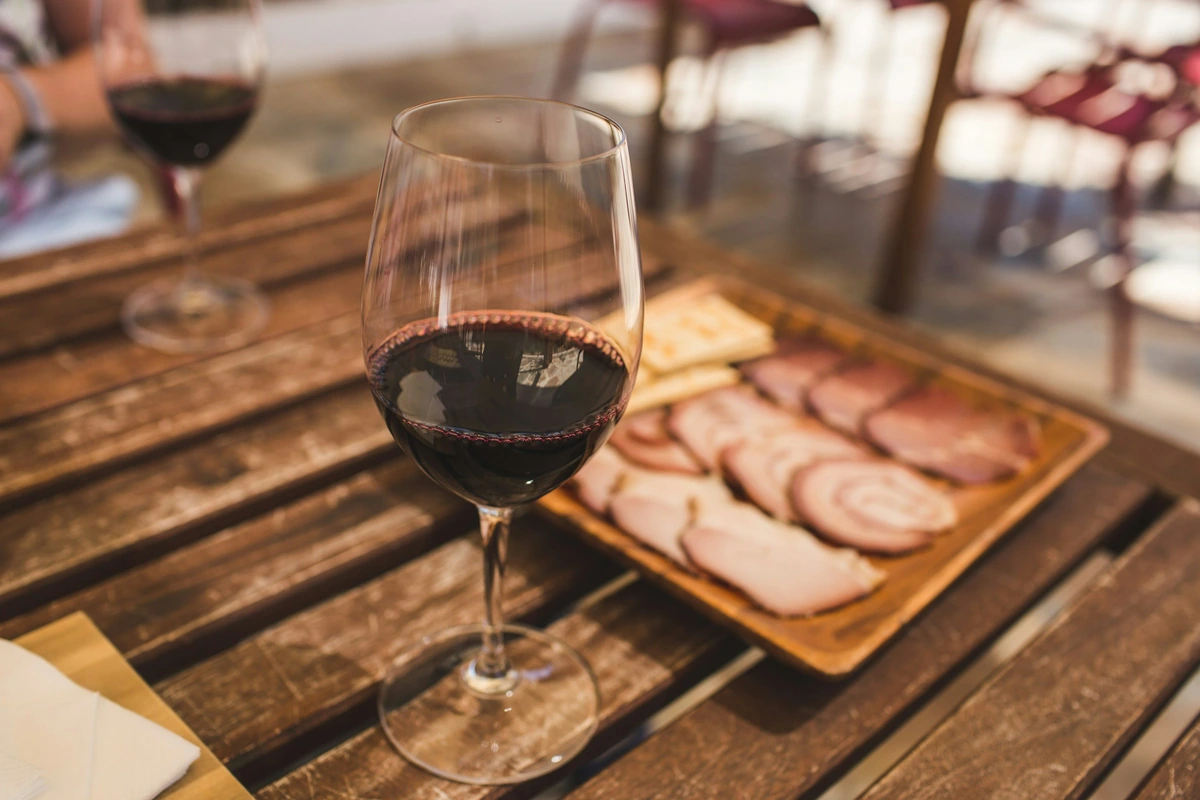 Taça de vinho tinto com charcutaria fatiada e torradas sobre madeira