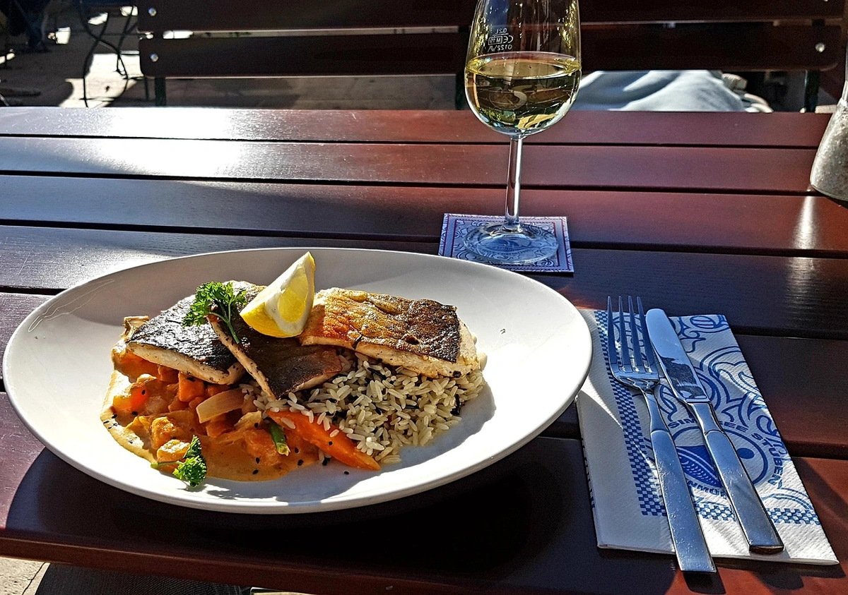 Peixe com legumes ao curry e arroz, acompanhado de taça de vinho branco