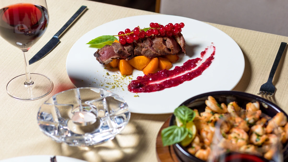 Prato com fatias de carne, molho e acompanhamentos, ao lado de uma taça preenchida de vinho tinto.