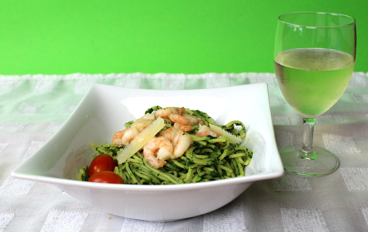 Massa com camarões e molho verde acompanhada de uma taça de vinho branco