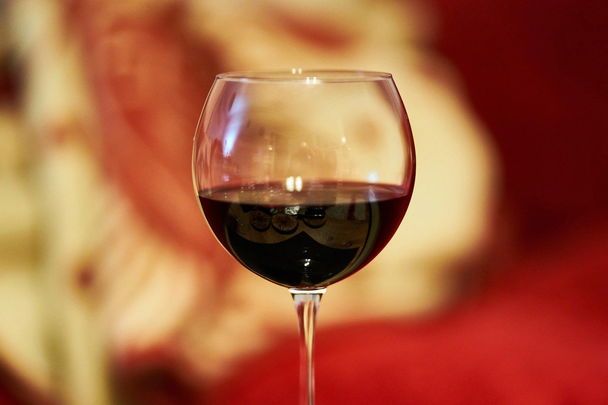 Detalhe de uma taça com vinho tinto escuro contra fundo desfocado em tons quentes.